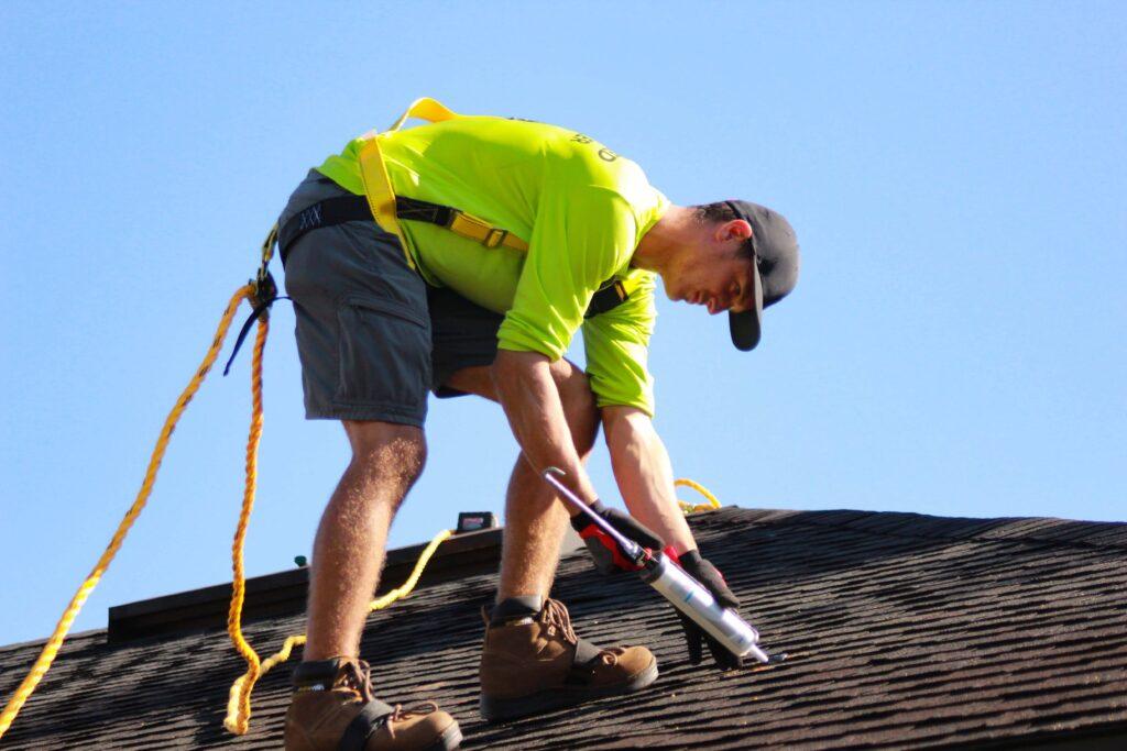 A man in a yellow shirt is working on a roof - Allen roofer and regular roof repairs and maintenance